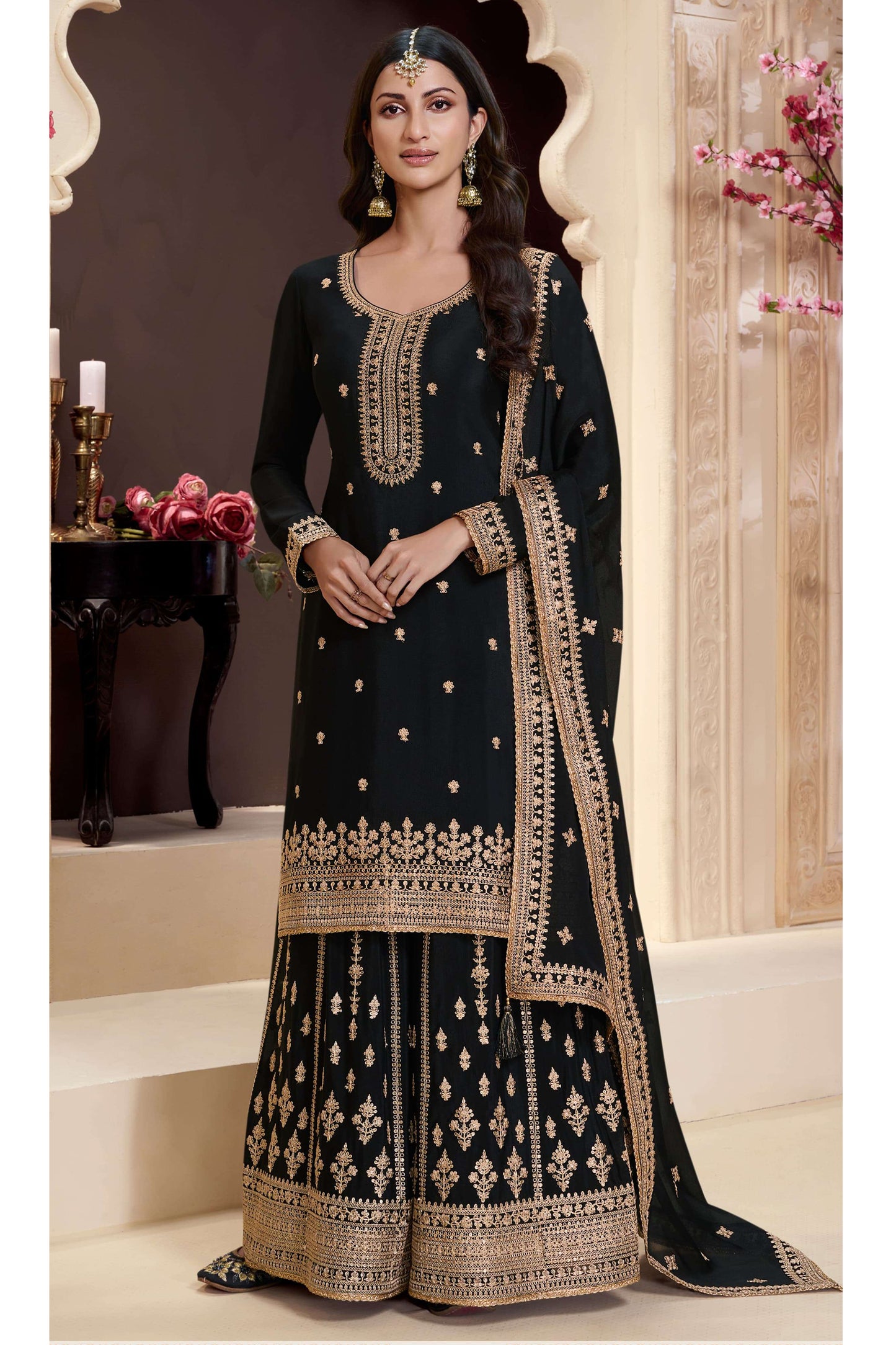 Woman wearing a black embroidered traditional outfit with gold details in an elegant setting.