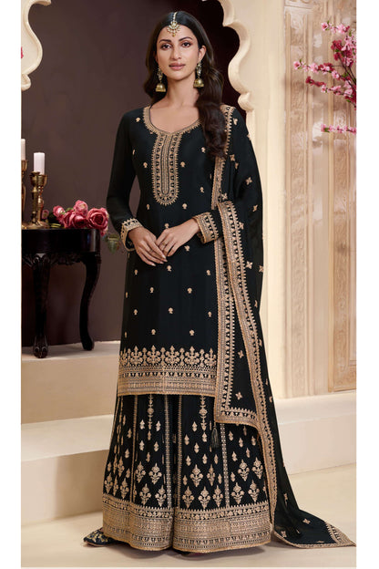 Woman wearing a black embroidered traditional outfit with gold details in an elegant setting.