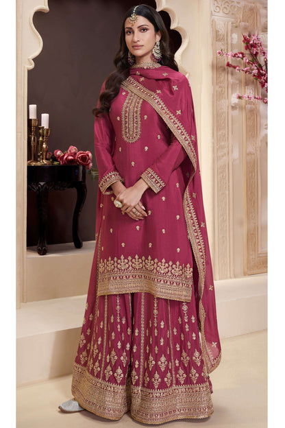 Woman wearing a pink traditional outfit with gold embroidery in an indoor setting.
