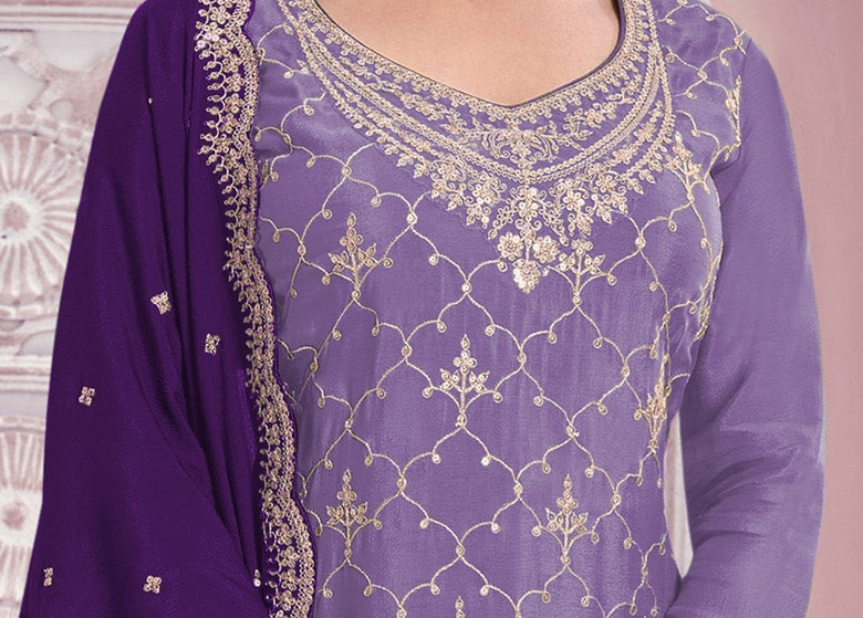 A close-up of a purple traditional outfit with intricate gold embroidery on the neckline and across the fabric, paired with a matching purple dupatta draped over the shoulder.