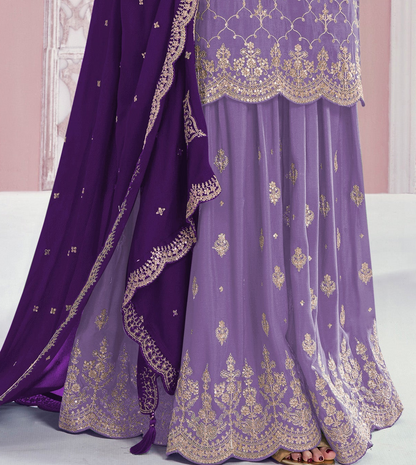 A close-up of a traditional Indian outfit featuring a lavender purple skirt with gold embroidery, a matching embroidered top, and a deep purple dupatta draped over the side.